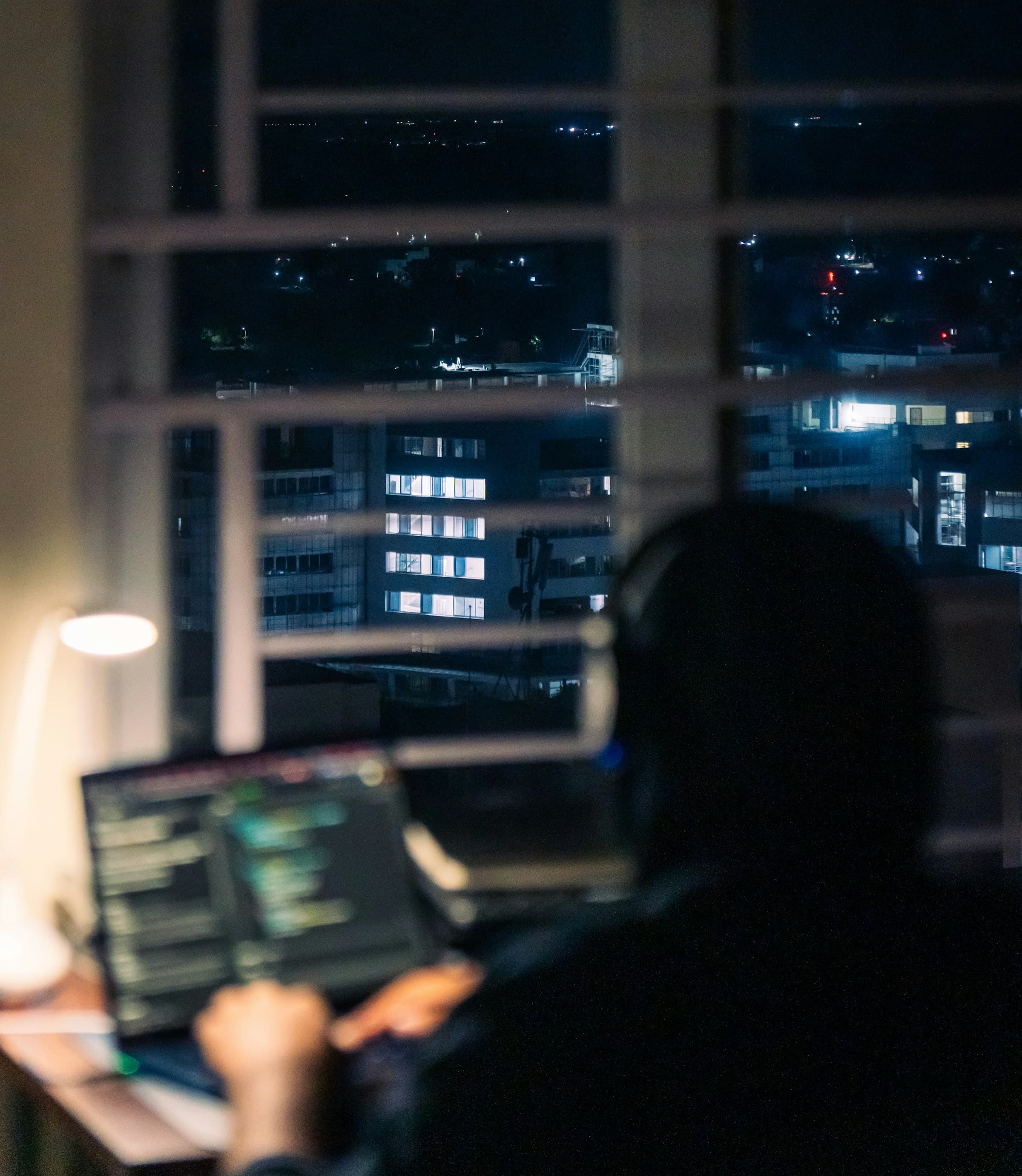 A person working late on a laptop, city lights visible through the window