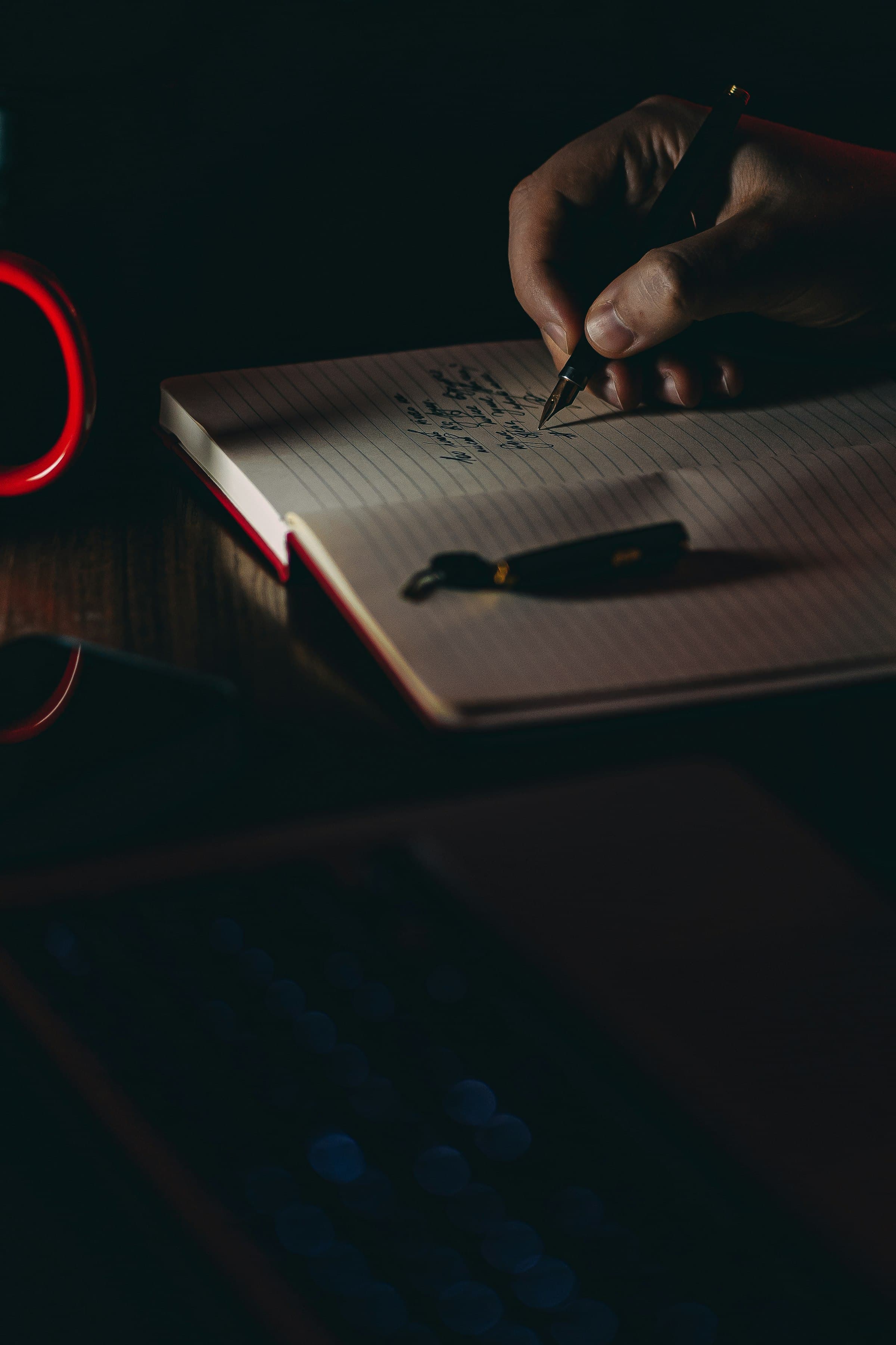 A hand writing notes with a fountain pen under a desk lamp